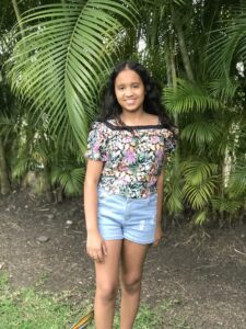 Young girl in a floral patterned blouse and shorts standing in front of tropical greenery