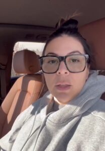 Woman wearing glasses and a gray sweatshirt sitting in a car
